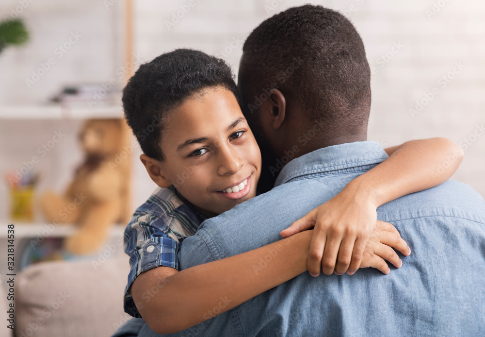 Obraz premium Teen Black Boy Embracing His Father With Love And Tenderness At Home