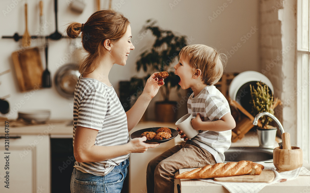 preparation of family breakfast. mother and child son cut bread  and eat cookies with milk in morning - obrazy, fototapety, plakaty 