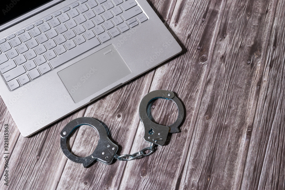 Handcuffs and laptop on wooden table. Piracy, internet hacking and punishment for cybercrime concept. Handcuffs and laptop on wooden table. Piracy, internet hacking and punishment for cybercrime concept.