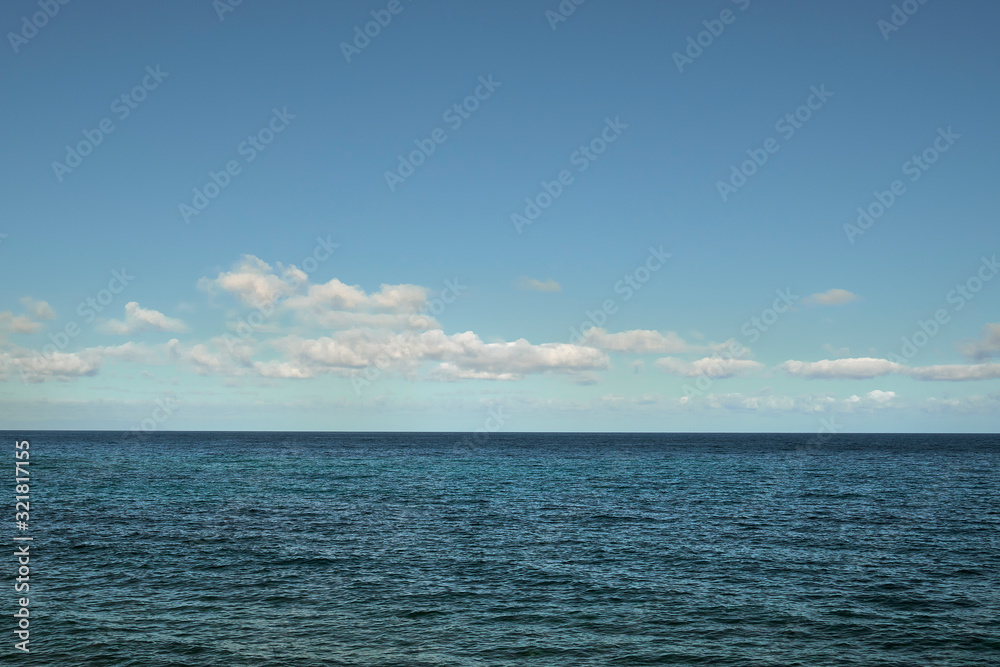 Image in which the calm sea is seen in the lower half and the sky in cyan and blue tones with white clouds in the upper half