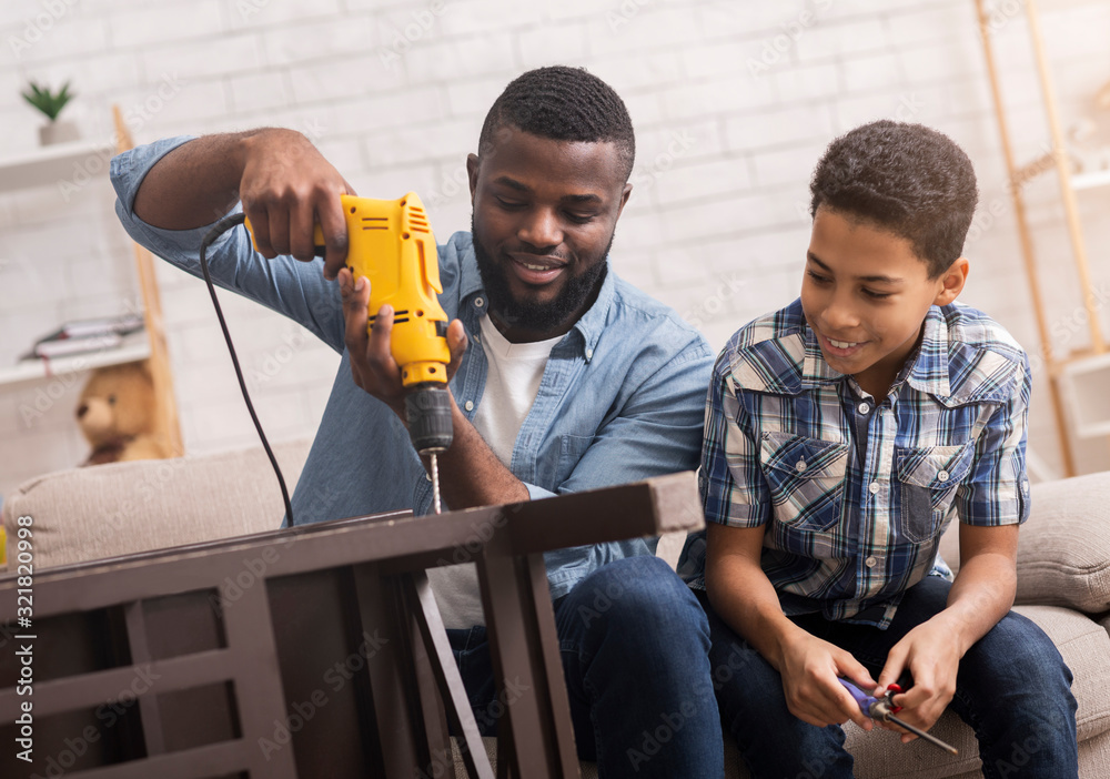 Black father teaching his son how to use drill perforator - obrazy, fototapety, plakaty 