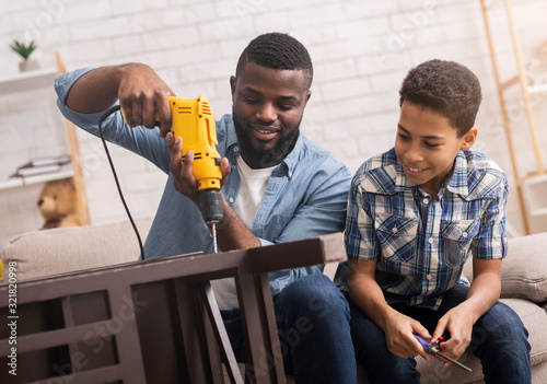 фотографія Black father teaching his son how to use drill perforator