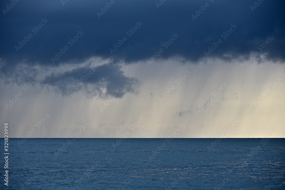 Spring seascape. Thunderstorm over the sea. Golden sunset on the horizon. A dark cloud from which it is raining against the backdrop of a golden sunset.
