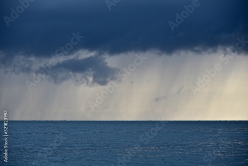 Spring seascape. Thunderstorm over the sea. Golden sunset on the horizon. A dark cloud from which it is raining against the backdrop of a golden sunset.