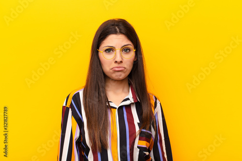 young pretty woman feeling sad and whiney with an unhappy look, crying with a negative and frustrated attitude against yellow wall photo