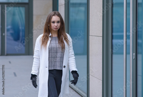 Young beautiful girl walking in a white coat in cloudy weather. Portrait photo session. Fashion.