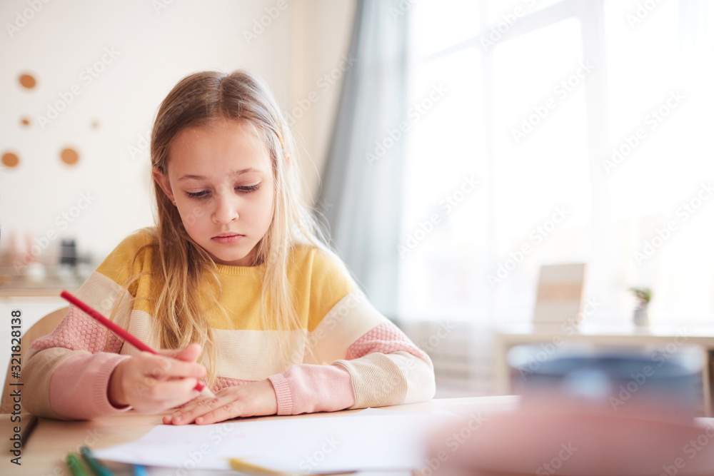Warm toned portrait of cute little girl drawing pictures or doing homework while sitting at table in home interior, copy space Warm toned portrait of cute little girl drawing pictures or doing homework while sitting at table in home interior, copy space