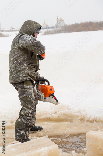 Worker in a green jacket with a hood with a chainsaw in his hands