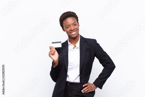 young pretty black womansmiling happily with a hand on hip and confident, positive, proud and friendly attitude holding a credit card photo