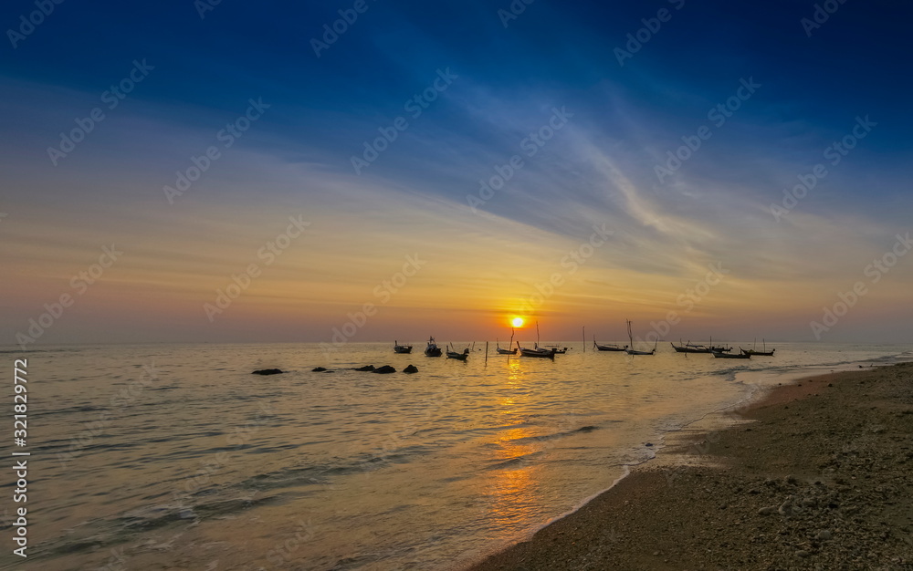 Fototapeta premium view seaside evening of fishing boats floating in the sea with orange sun light and blue sky background, sunset at Klong Hin Beach, Ko Lanta island, Krabi, southern of Thailand.