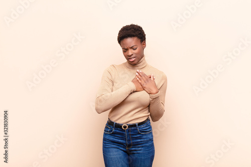 young pretty black womanlooking sad, hurt and heartbroken, holding both hands close to heart, crying and feeling depressed photo