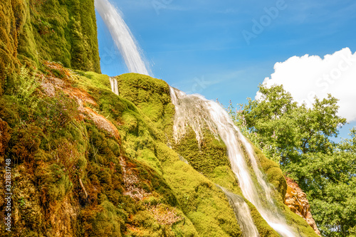 Wasserfall auf bemoostem Felsen vor blauem Himmel