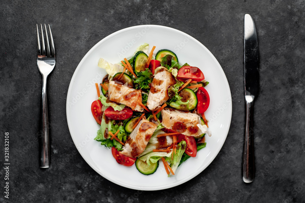 a plate of salad of tomato, chicken, cucumber, carrots, soy sauce in a plate on a stone background a plate of salad of tomato, chicken, cucumber, carrots, soy sauce in a plate on a stone background