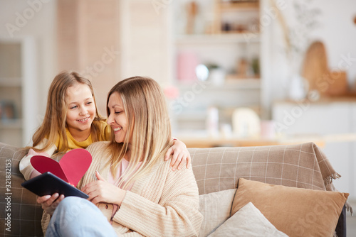 Warm toned portrait of cute little girl giving heart-shaped card to happy mother on Mothers day or Valentines day, copy space