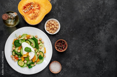 a plate of avocado salad, chickpeas, pumpkin, cucumber, poached egg in a plate on a stone background with copy space for your text