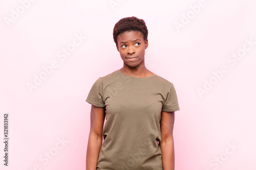 young pretty black womanlooking puzzled and confused, wondering or trying to solve a problem or thinking against pink wall photo