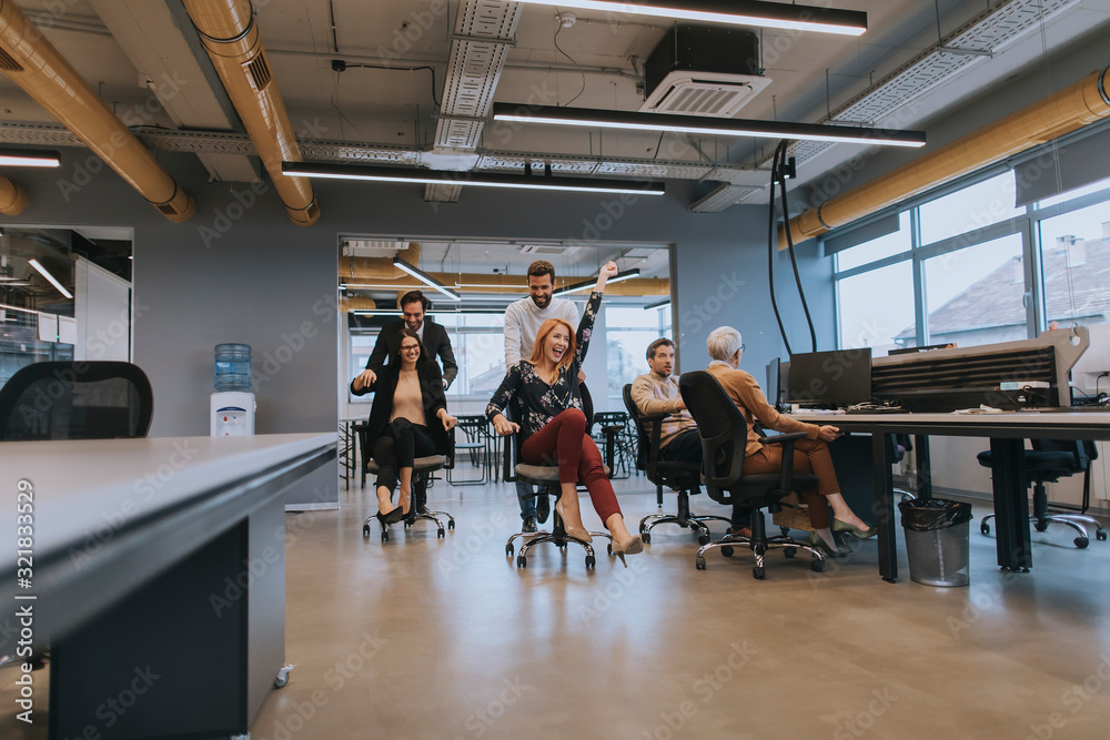 Young business people in smart casual wear having fun while racing on office chairs and smiling Young business people in smart casual wear having fun while racing on office chairs and smiling