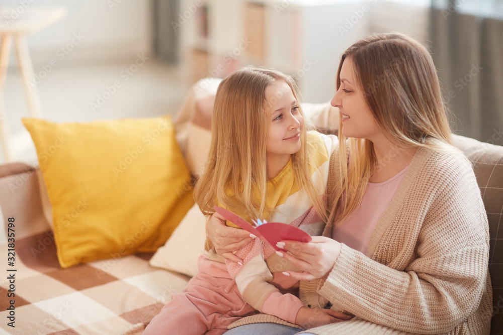 Portrait of blonde little girl embracing mom while celebrating Mothers day together sitting on cozy couch at home, copy space
