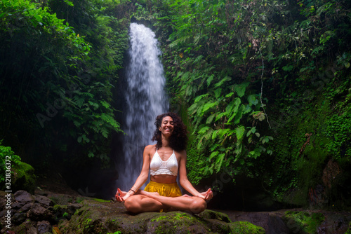 outdoors portrait of young attractive and happy hipster girl doing yoga at beautiful tropical waterfall meditating enjoying freedom and   nature in wellness and zen lifestyle