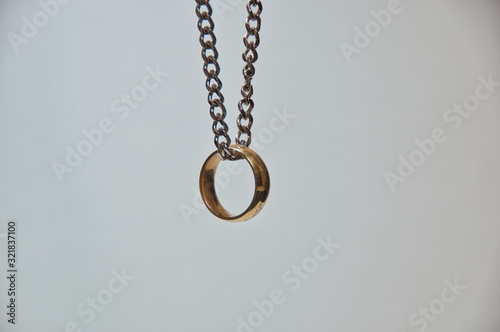 Golden ring hanging in the air from chrome chain on white background.