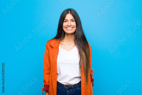 young pretty latin woman looking happy and goofy with a broad, fun, loony smile and eyes wide open against flat wall photo