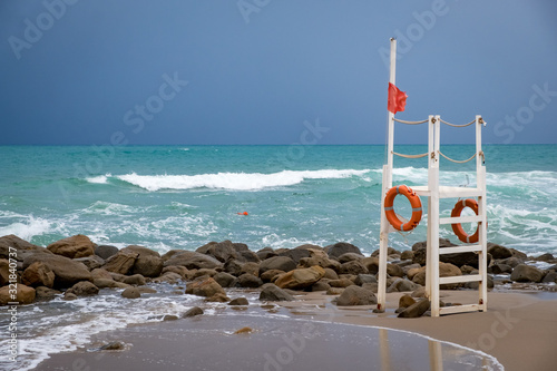 lifeguard tower on an empty beach in Cefalu during a storm. Stone coast, spray from the waves, blue water. Sicily, Italy photo