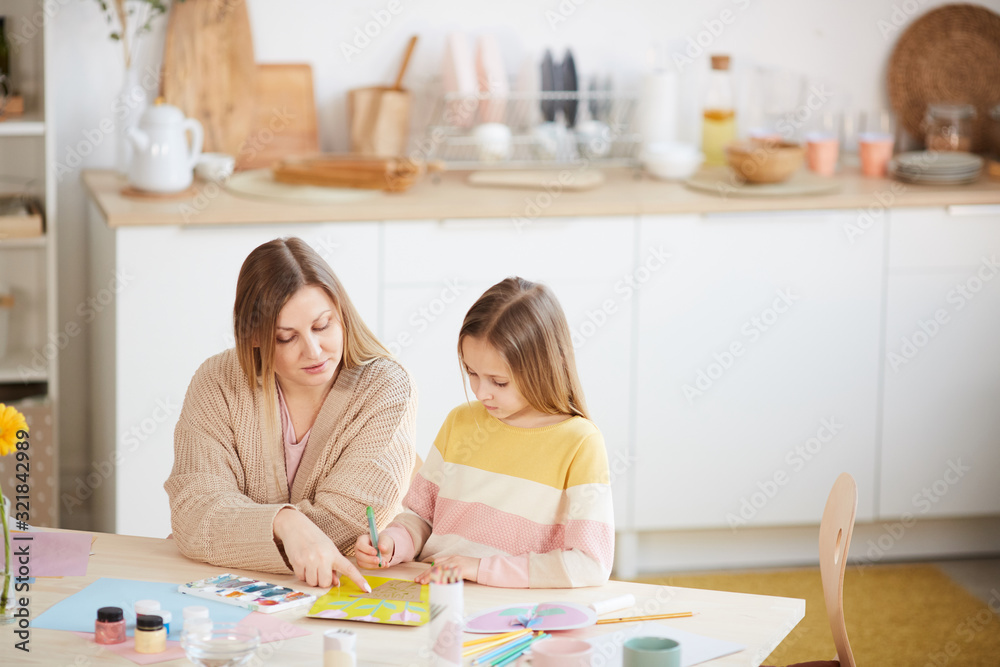 Fototapeta premium High angle portrait of mature mother helping cute daughter with art and craft project in home interior, copy space