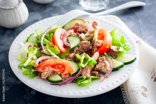 Salad with tuna and fresh tomatoes, cucumber and onions, on a white plate, selective focus