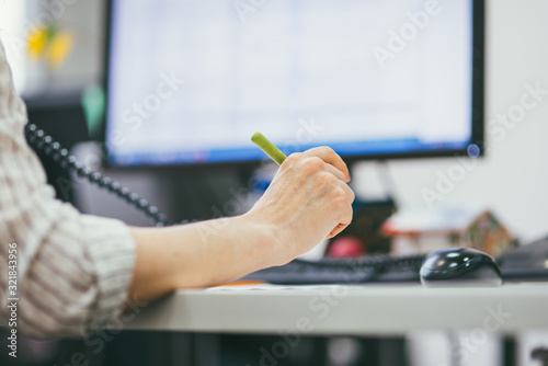 Photography Close-up of a woman's hand with a pen on the background of the monitor