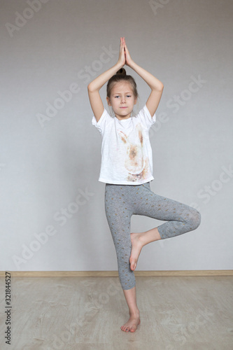 A little cute girl practices a yoga pose indoors. The child does yoga and gymnastic exercises.