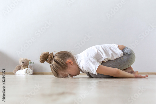 A little cute girl practices a yoga pose indoors. The child does yoga and gymnastic exercises.