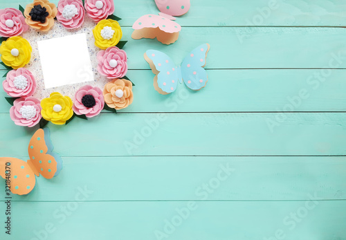 Decorative frame with colorful felt flowers and beautiful paper butterflies. Top view, copy space for your text on a blue wooden table. Background for Birthday, March 8, Valentine's Day