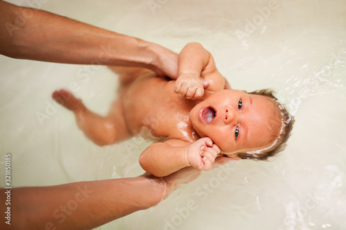 Little charming girl bathes in warm water in the bathtub in the caring hands of an unidentified mother. The concept of love and care for little innocent children