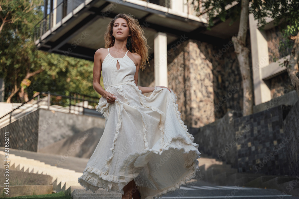 Beautiful young girl woman with long hair in a white elegant dress of the bride walks in a summer park