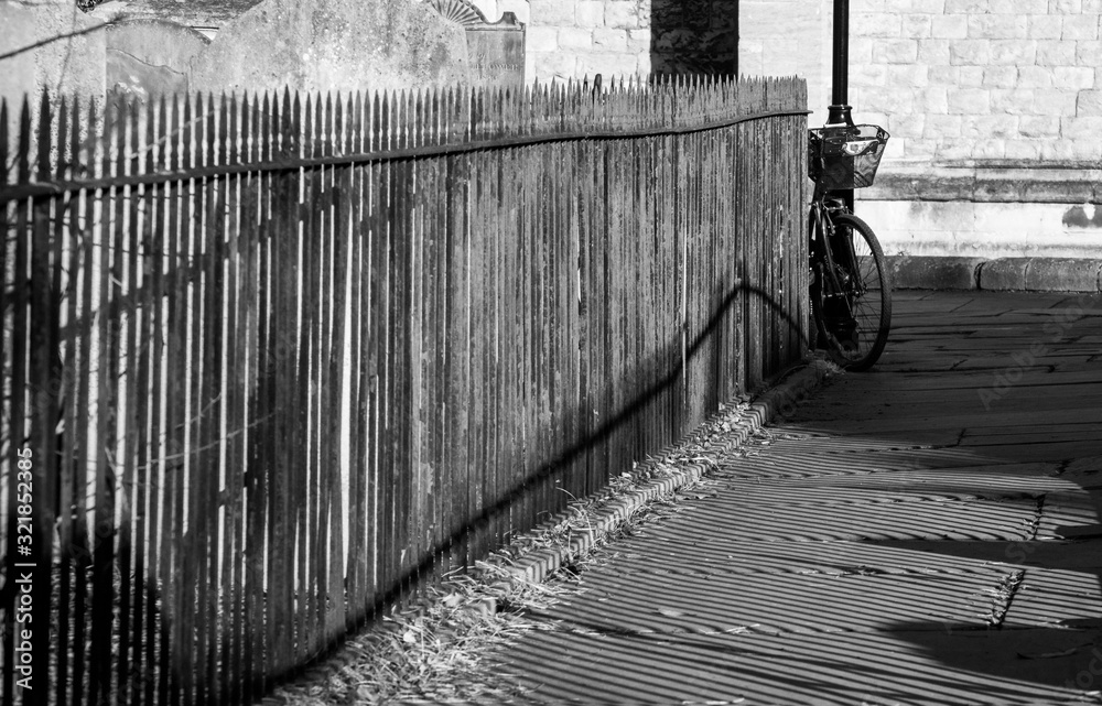 Fototapeta premium Close up of railings and their shadows beside a pathway at St Nicholas Church, Chiswick, London UK, photographed with high contrast in late afternoon on a sunny day in February.