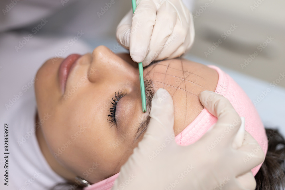 Naklejka premium The girl beautician marks with the help of thread eyebrow tattoo. Permanent makeup. Permanent tattooing of eyebrows.