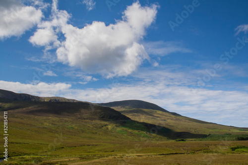 Green Irish hills with bright blue sky and puffy clouds casting deep shadows.