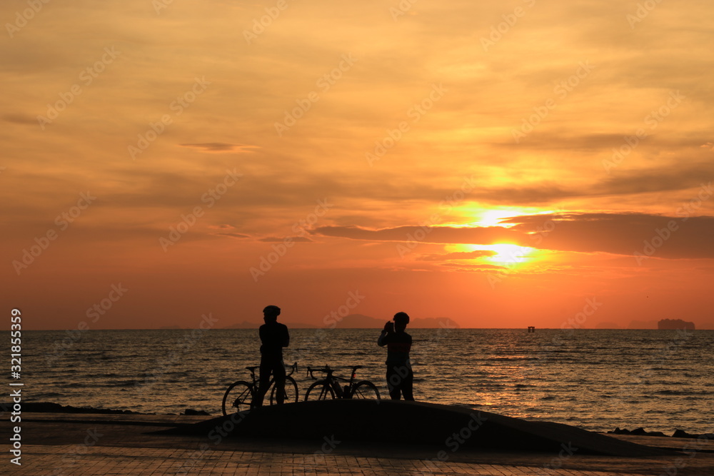 The silhouette of lovers riding bicycles and watching and photographing the sunrise on the beach at dawn