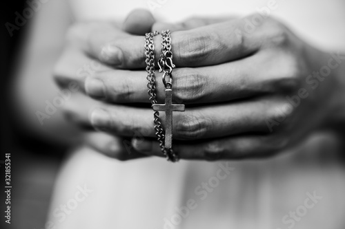 Black and white of woman hands praying holding a beads rosary with Jesus Christ in the cross or Crucifix on black background.