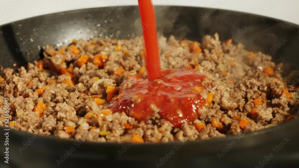 Tomato, bolognese sauce being added to ground or mince beef in black pan. Italian food concept Tomato, bolognese sauce being added to ground or mince beef in black pan. Italian food concept