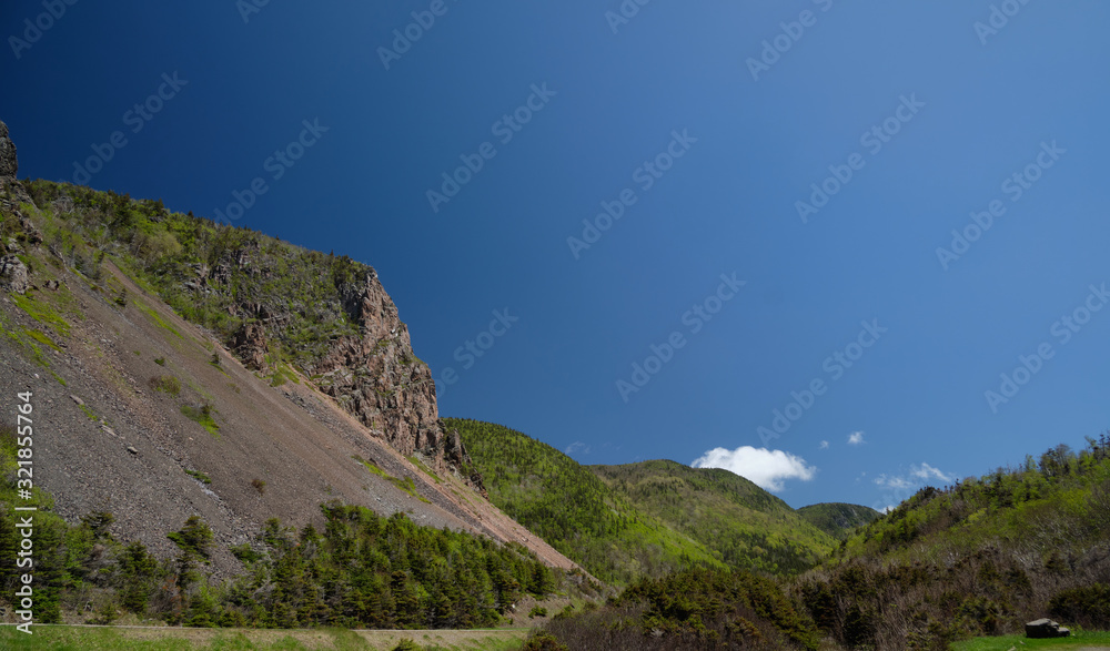 Landscape of hills, rocky on the foreground and covered by green forest on the background. Beautiful blue sky with several clouds.