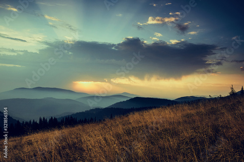 Beautiful landscape in the mountains at sunrise with haze and cloudy sky. View of the magnificent natural scenery of mountains hills. Filtered image: cross processed retro effect.