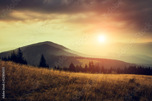 Beautiful landscape in the mountains at sunrise with haze and cloudy sky. View of the magnificent natural scenery of mountains hills. Filtered image: cross processed retro effect.