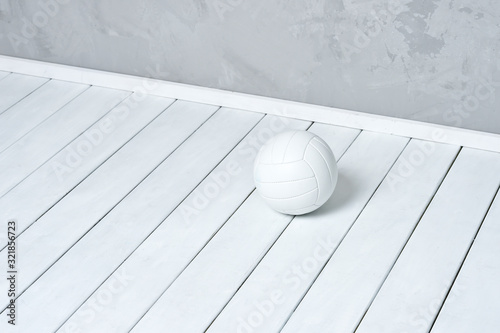 White volleyball lying on wooden surface near grey wall with copy space