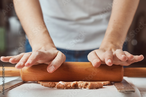 Female hands rolling dough on the table, closeup. Woman making dough for baking in kitchen