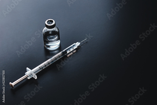 Medical syringe and ampoule with medicine on the black background, top view with copy space. Vaccination and virus protection concept photo