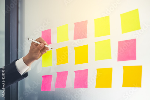 Close up hand businessman writing sticky notes on glass wall in office.