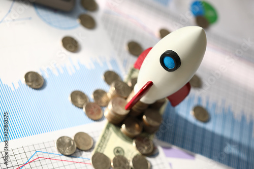 Investment profitability planning and analysis. Model space rocket stands on table next to coins. Calculation attractiveness financial project. Profitability analysis and startup promotion. © H_Ko