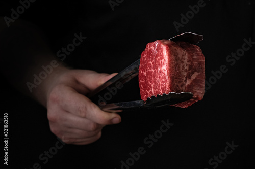 Raw filet Mignon steak in tongs in hand, cooking meat on the grill photo