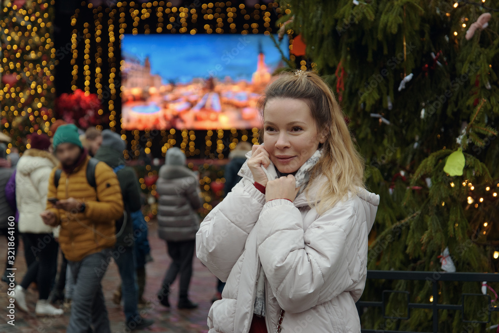Smiling young beautiful European woman in the middle of decorated old town European Christmas square. She is happy to spend her winter holidays in Tallinn.